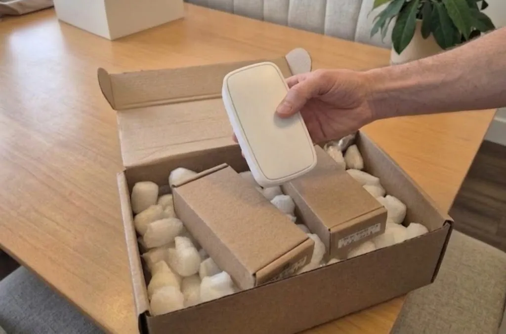 En hvid sensor løftes op af en åben leveringskasse.
